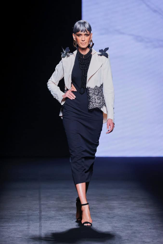 Modelo en la pasarela con vestido negro ajustado de Malne y chaqueta corta color marfil con detalles de encaje negro.