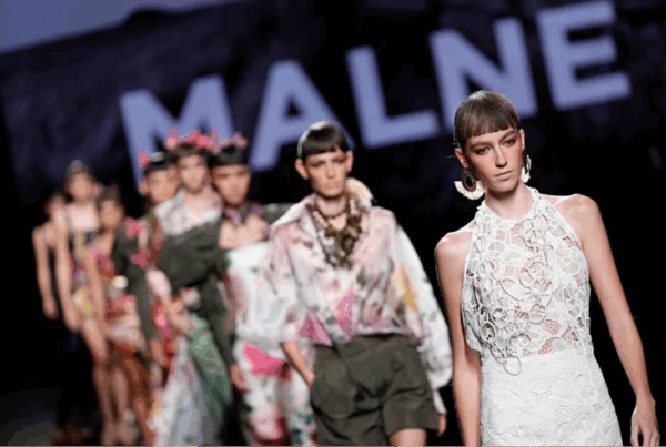 Desfile de moda de autor en pasarela, modelos caminando con vestidos de alta costura bajo focos.