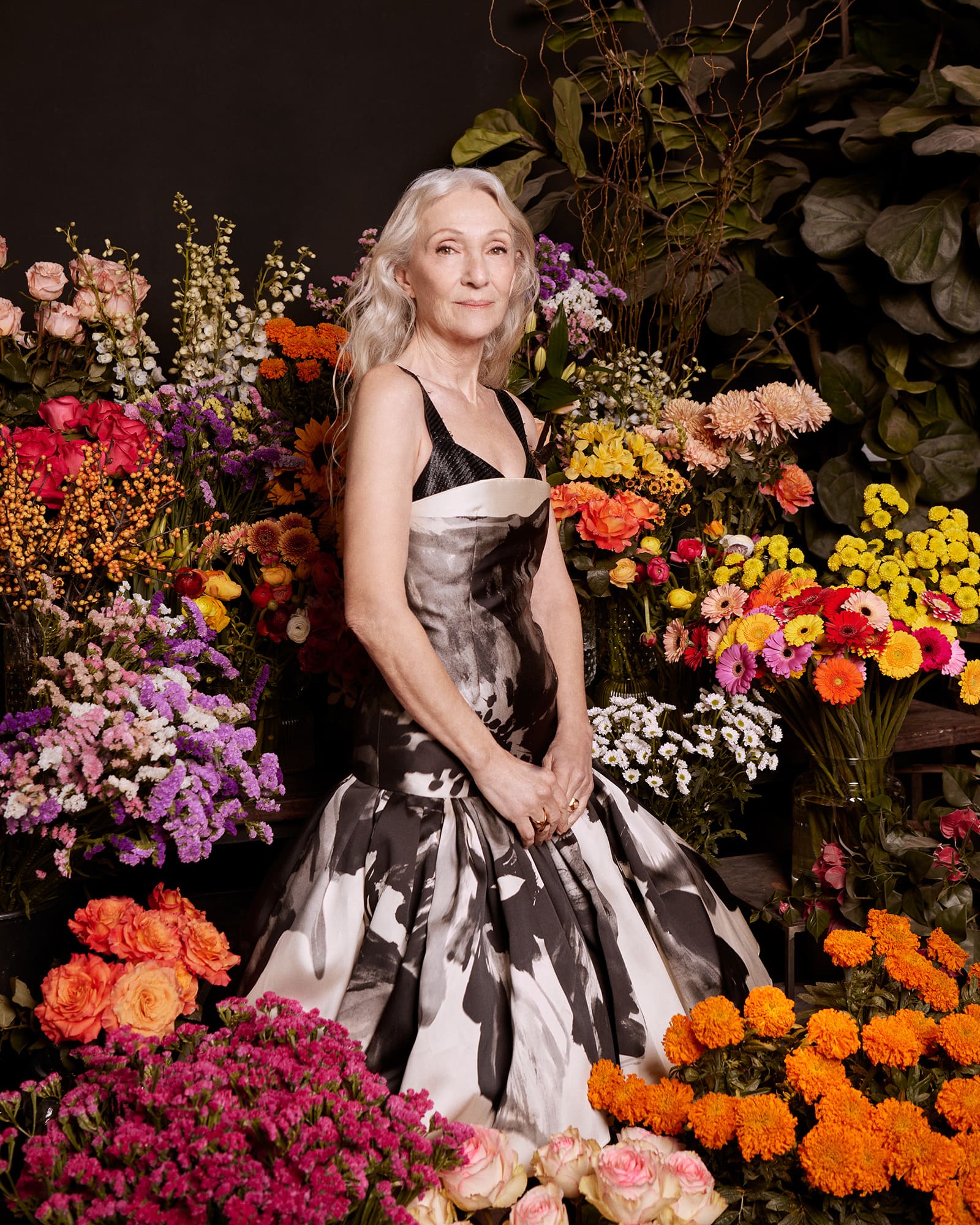 Mujer posa con un vestido elegante de estampado blanco y negro rodeada de abundantes arreglos florales de colores.