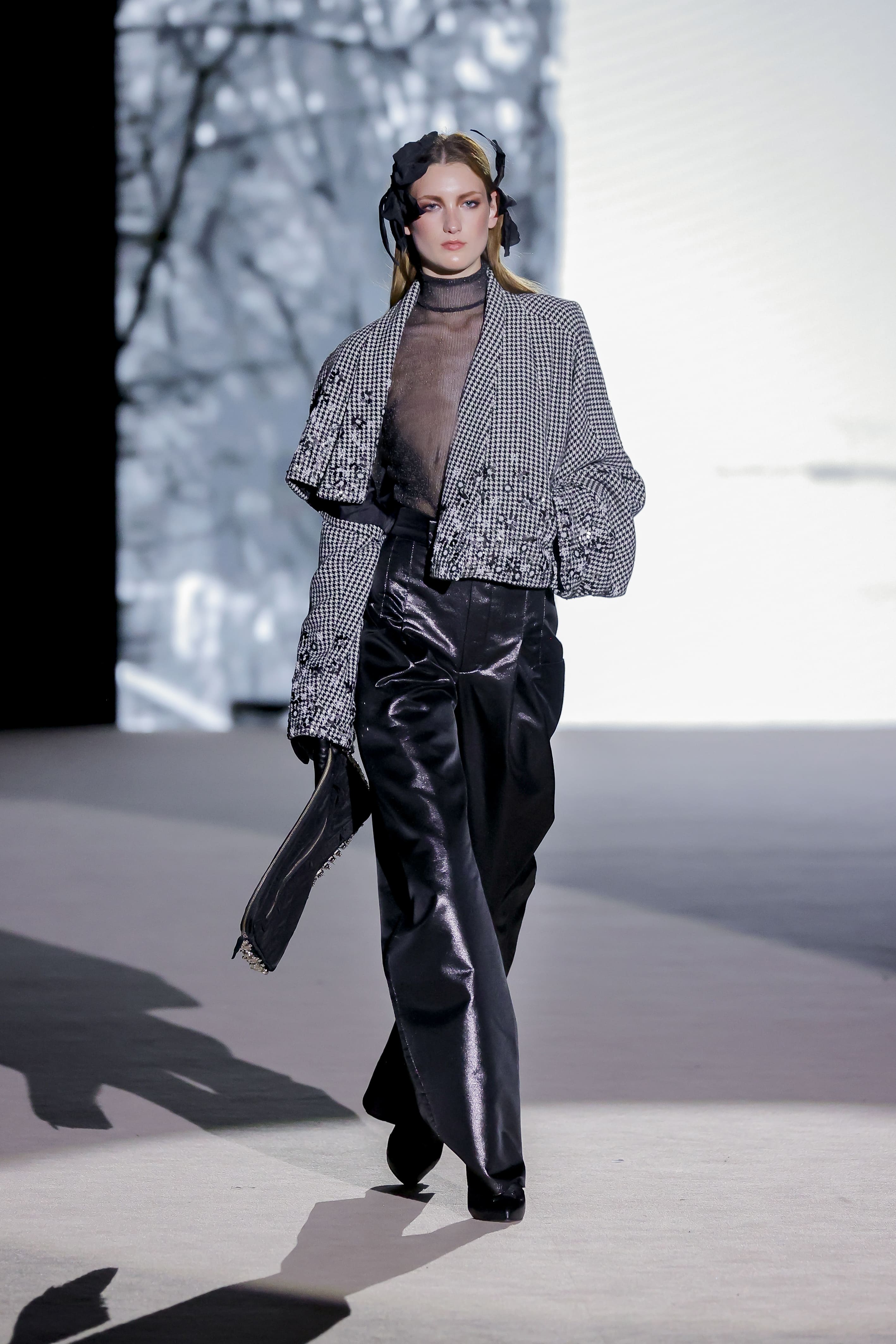 Modelo con chaqueta de pata de gallo y pantalón negro brillante de Malne en la Mercedes-Benz Fashion Week Madrid marzo de 2026 con bolso.