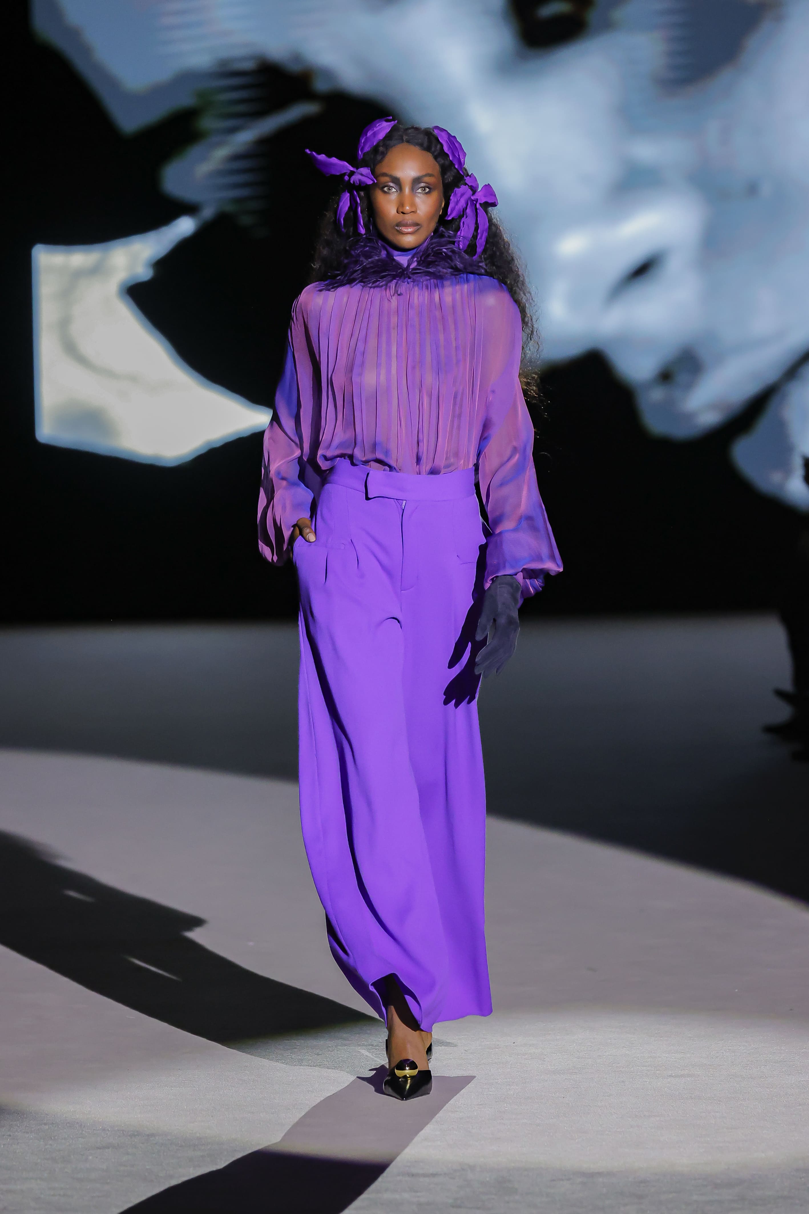 Modelo con conjunto púrpura de blusa plisada y pantalón de Malne en la Mercedes-Benz Fashion Week Madrid marzo de 2026 con tocado a juego.