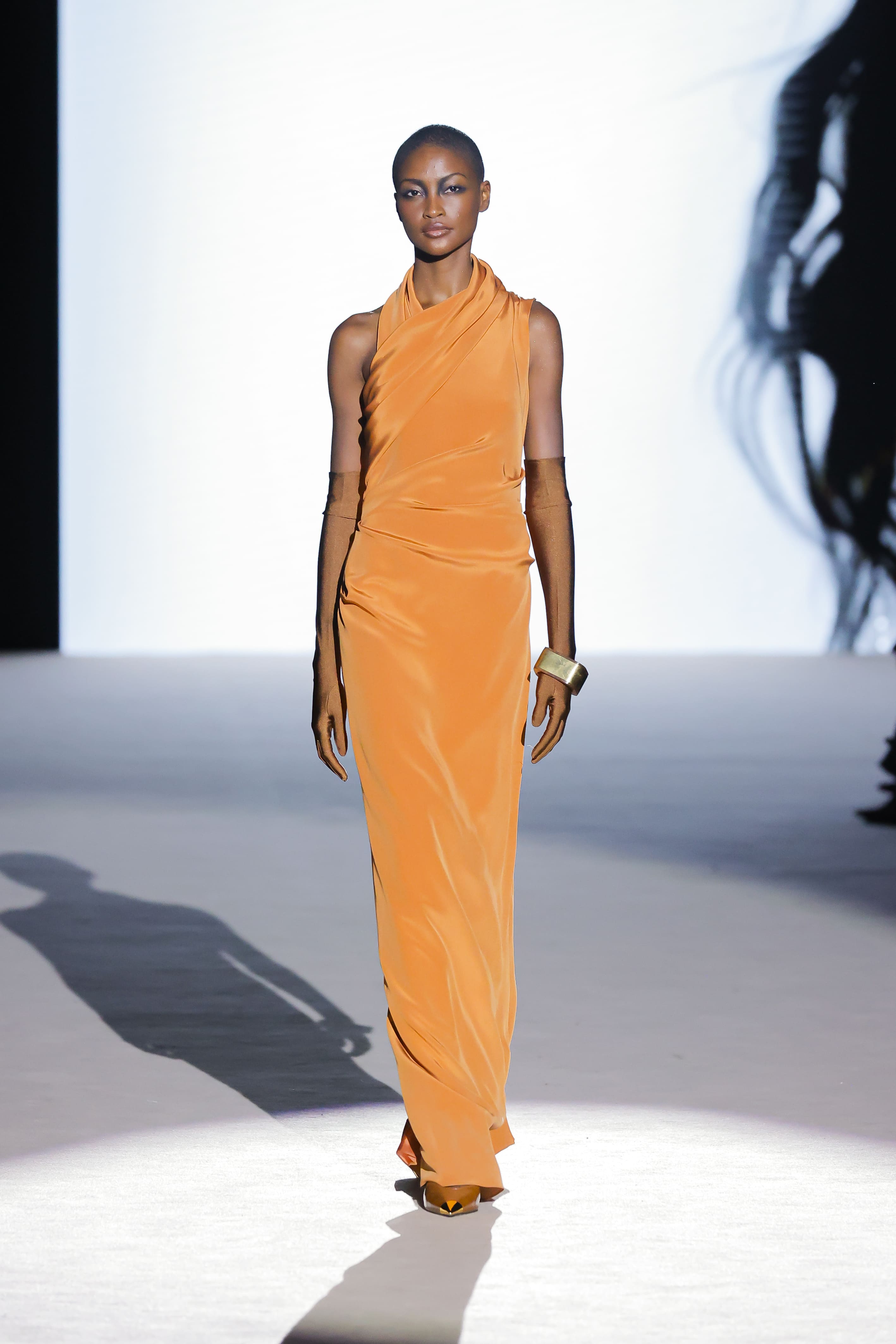 Modelo con vestido largo naranja de corte minimalista de Malne en la Mercedes-Benz Fashion Week Madrid marzo de 2026 con guantes largos.