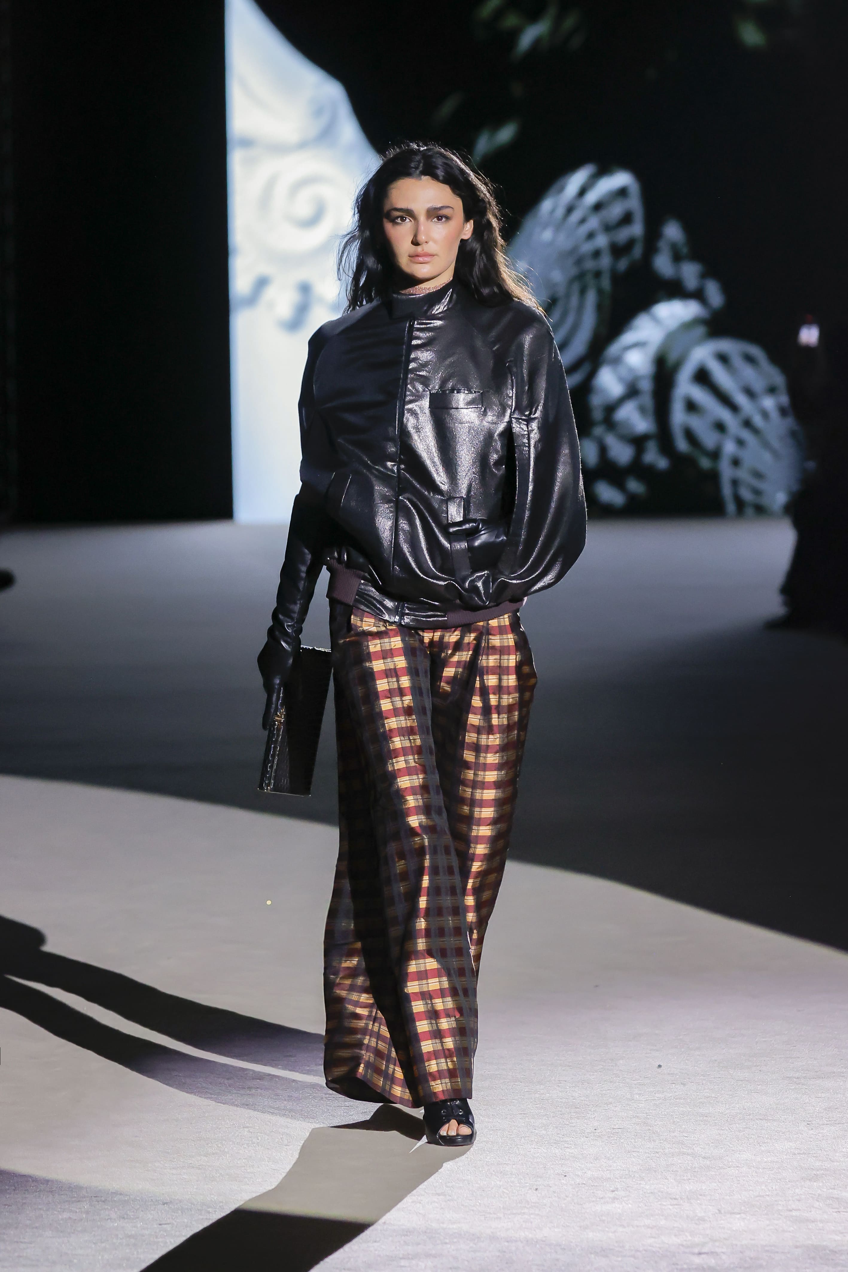 Modelo con chaqueta negra de cuero y pantalón de cuadros de Malne en la Mercedes-Benz Fashion Week Madrid marzo de 2026 con bolso de mano.
