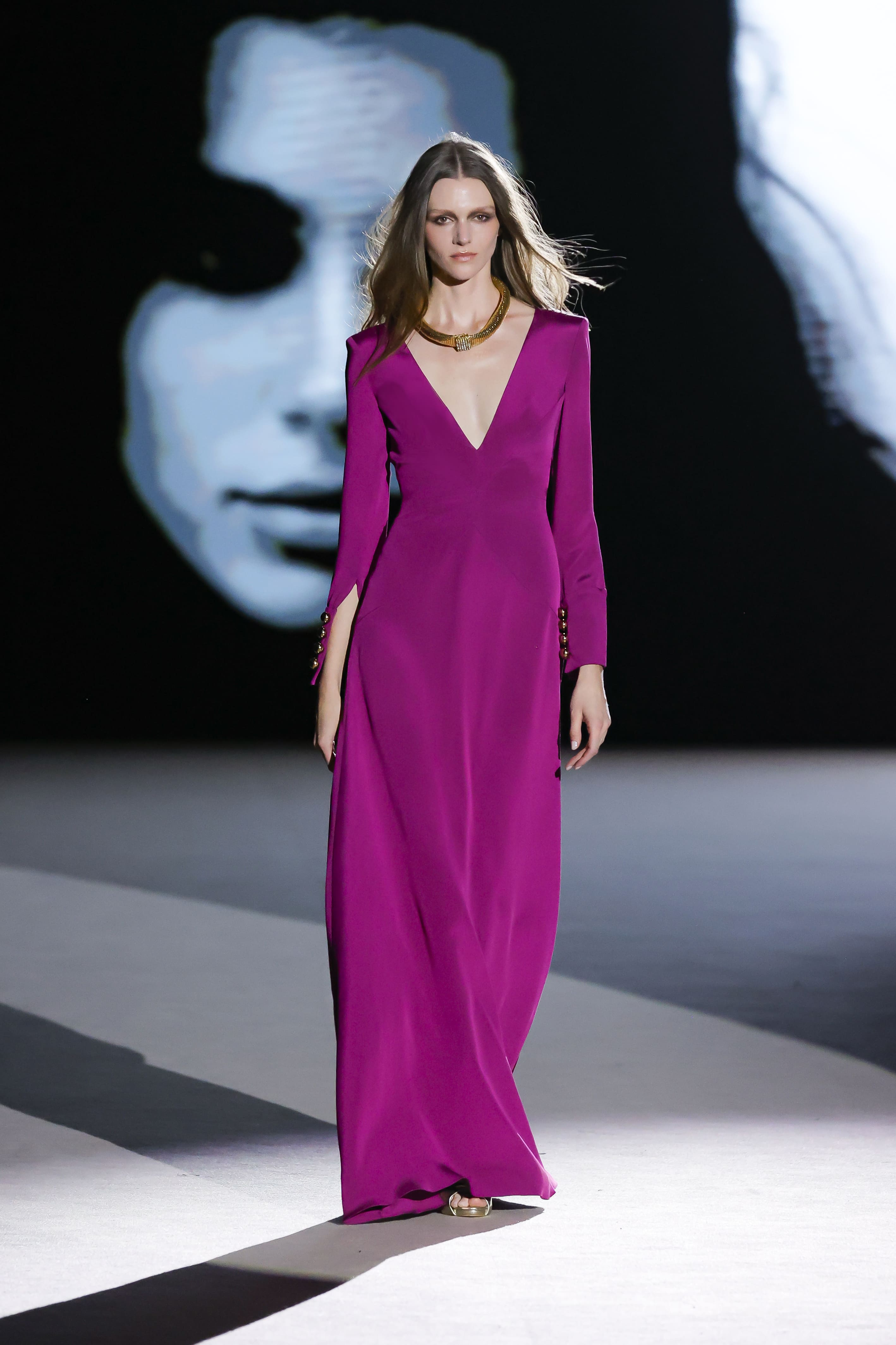 Modelo desfilando con vestido largo morado de escote en pico de Malne en la Mercedes-Benz Fashion Week Madrid marzo de 2026 con collar dorado.