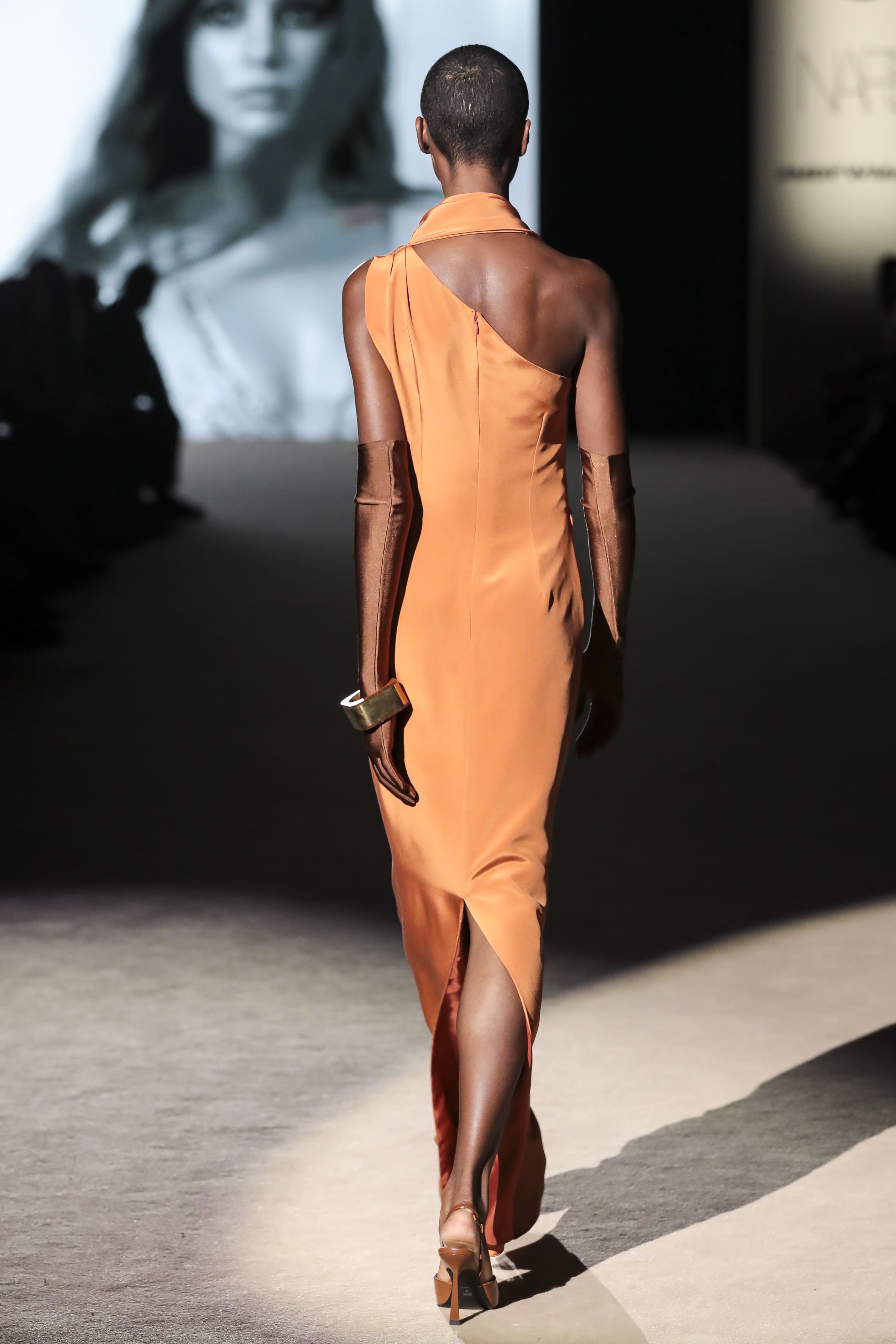 Modelo desfilando de espaldas con vestido naranja de corte minimalista de Malne en la Mercedes-Benz Fashion Week Madrid marzo de 2026 con guantes largos.