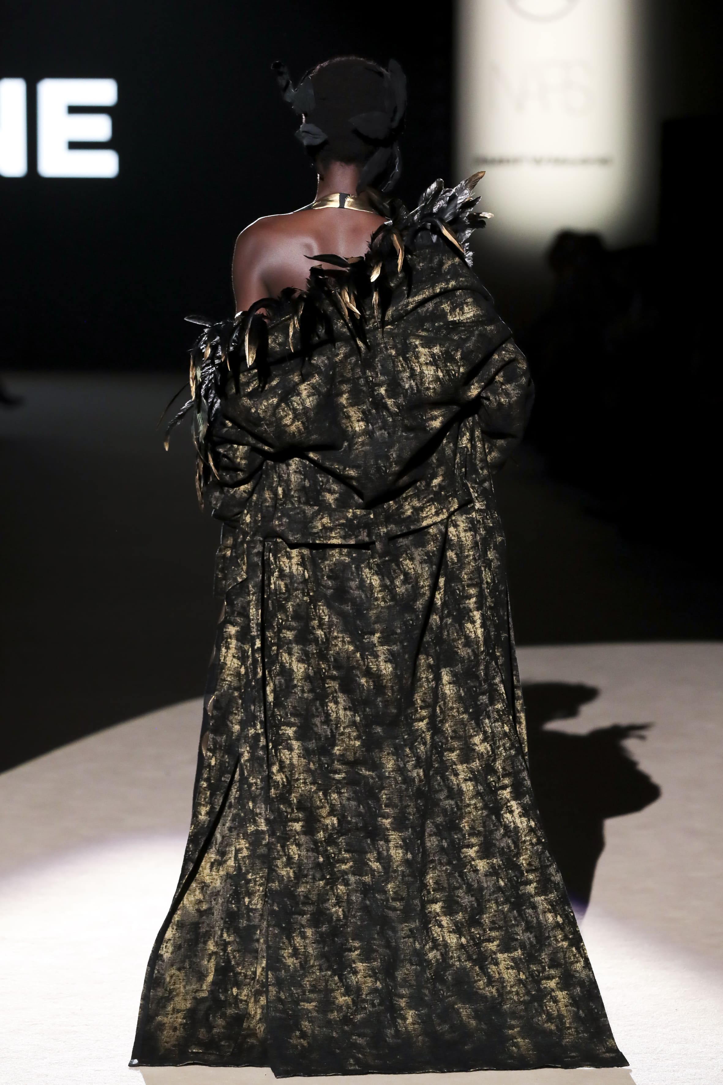 Modelo desfilando de espaldas con abrigo negro y dorado con detalles de plumas de Malne en la Mercedes-Benz Fashion Week Madrid marzo de 2026.