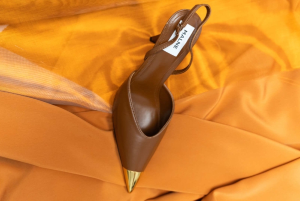 Zapato de tacón Malne destalonado marrón con punta dorada sobre tela de seda naranja brillante.